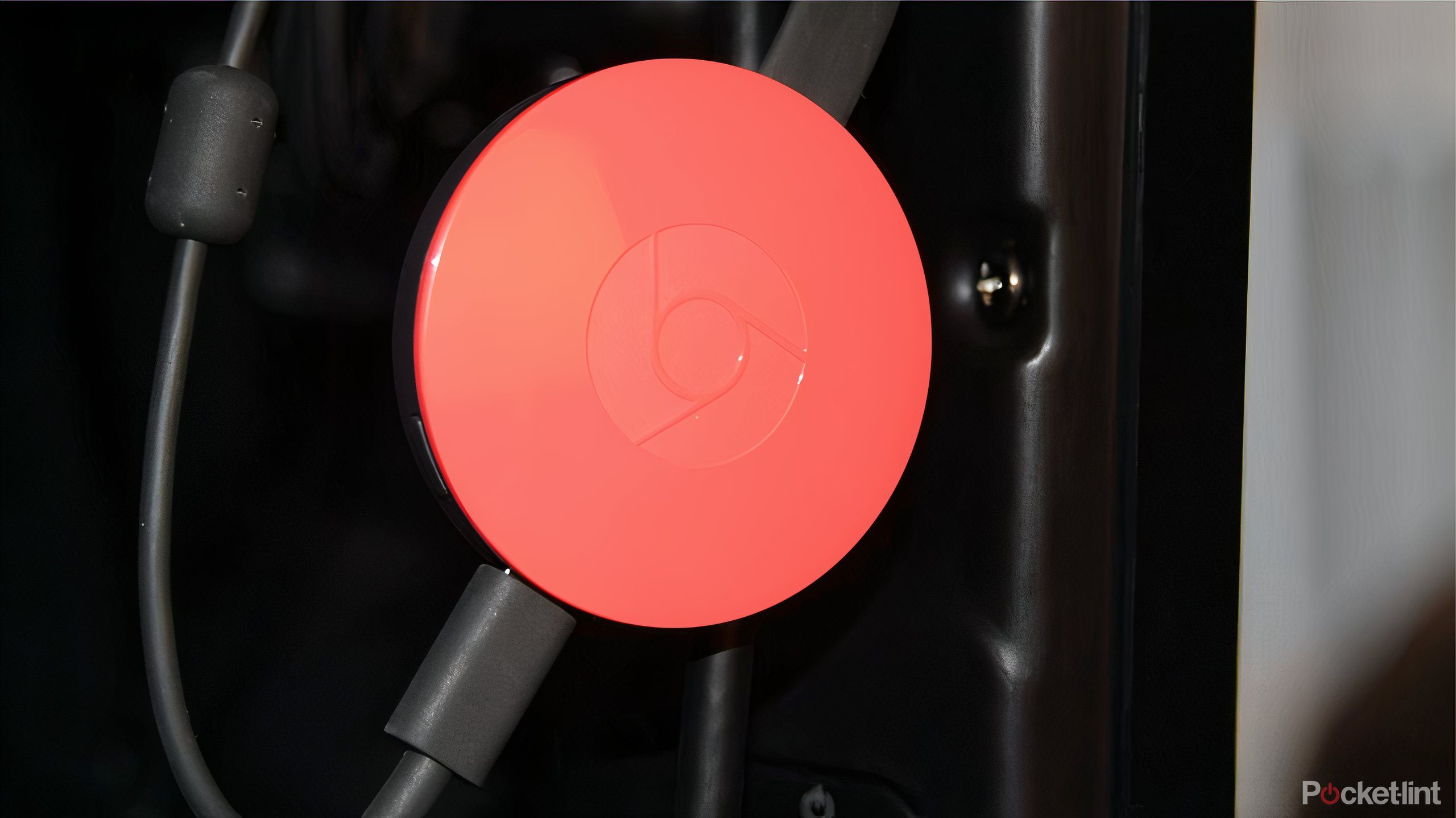 A red second generation Chromecast plugged into a TV.