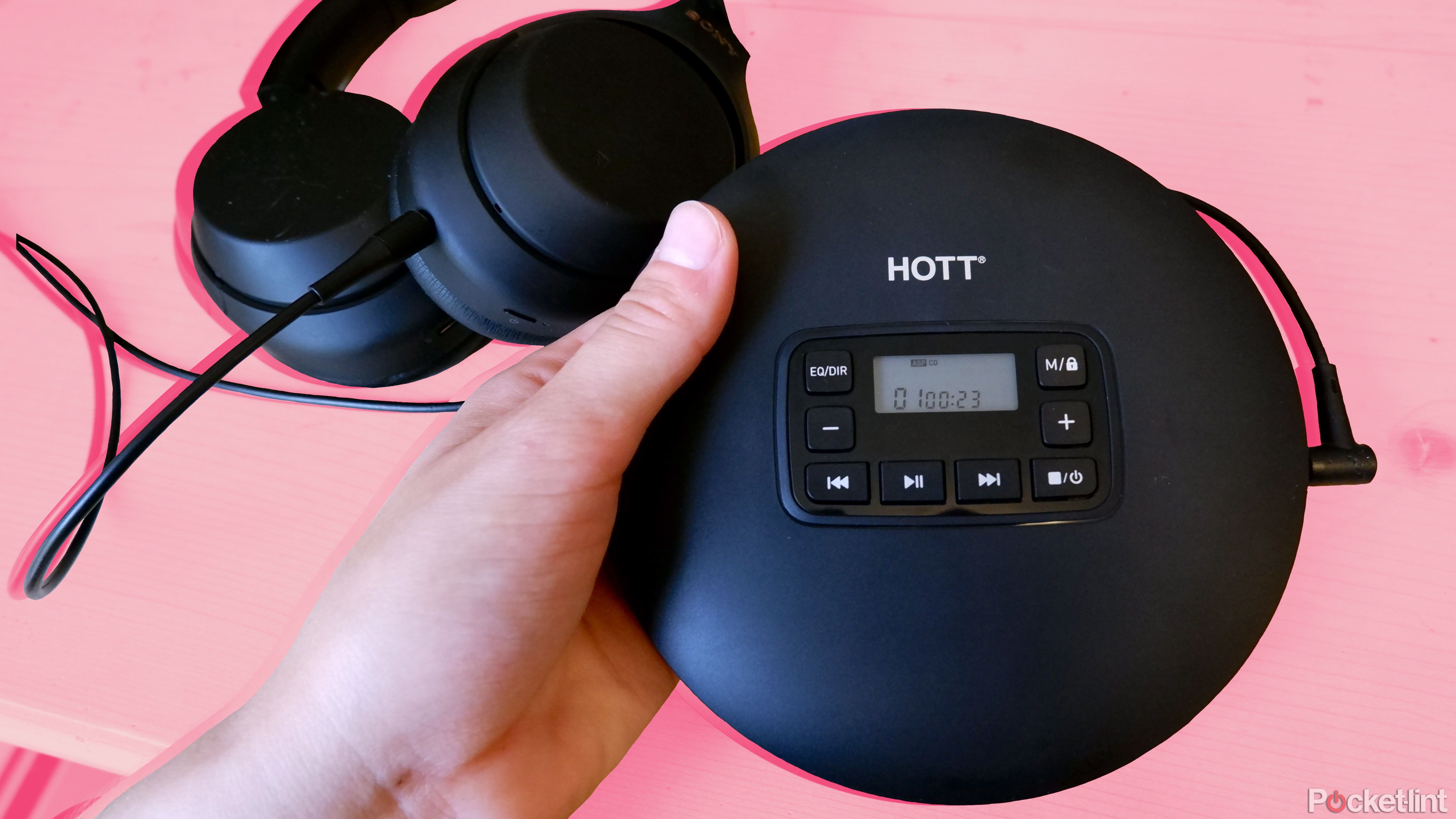 Hott CD204 being held above a wooden desk with over-ear headphones plugged in