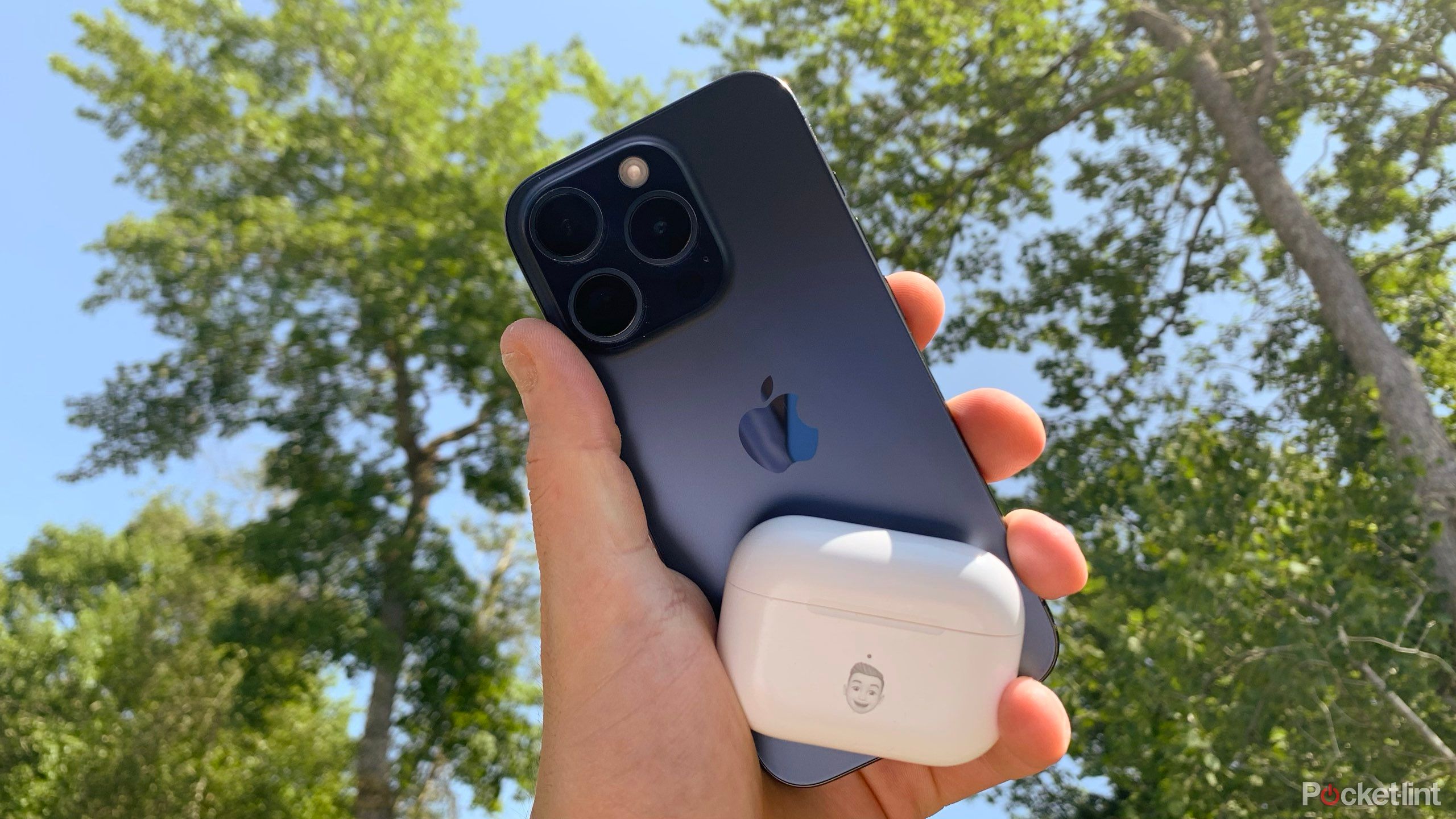 A blue iPhone 15 Pro held in a hand with closed AirPods Pro. 