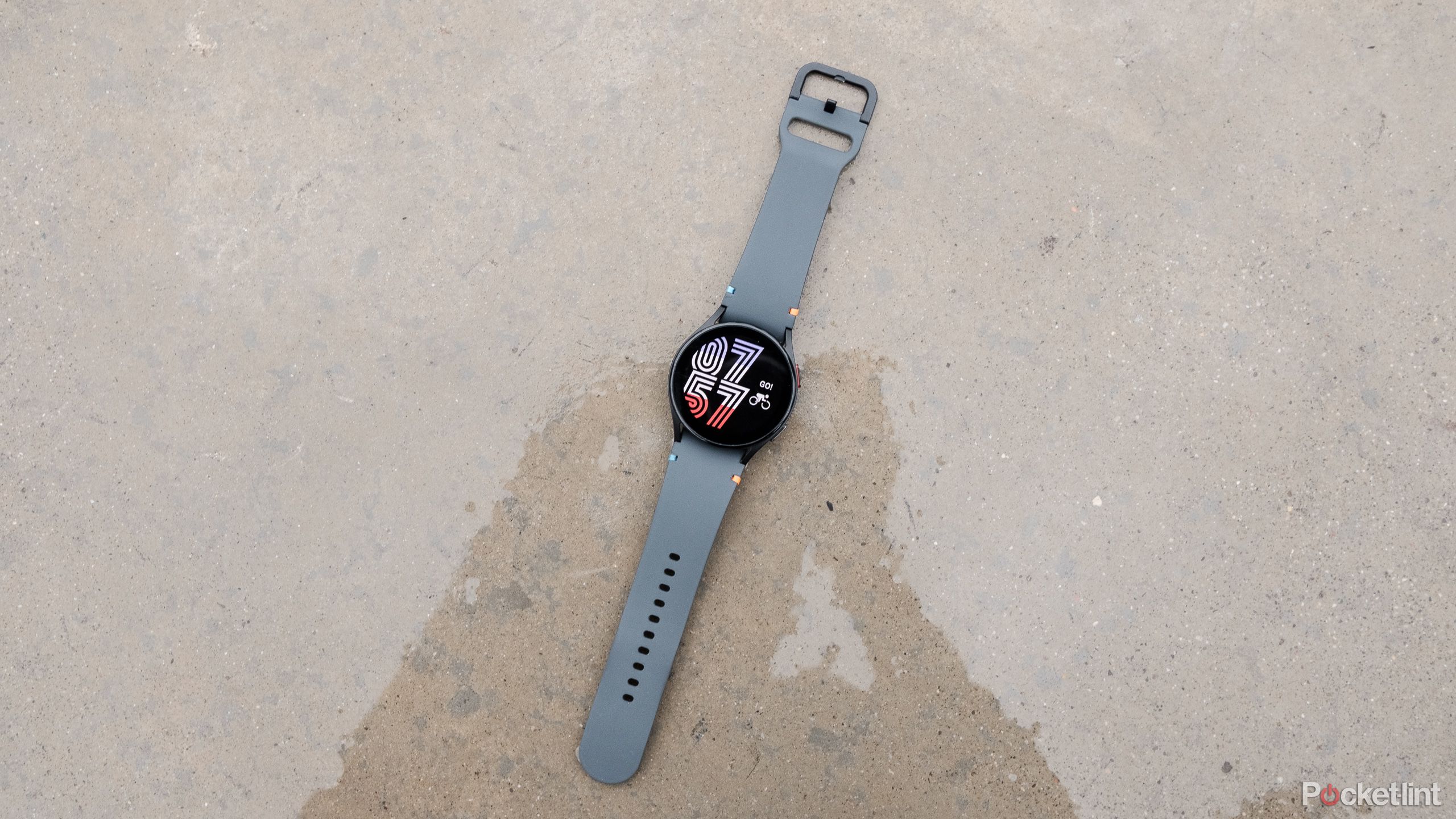 A black Samsung Galaxy Watch FE resting in a puddle