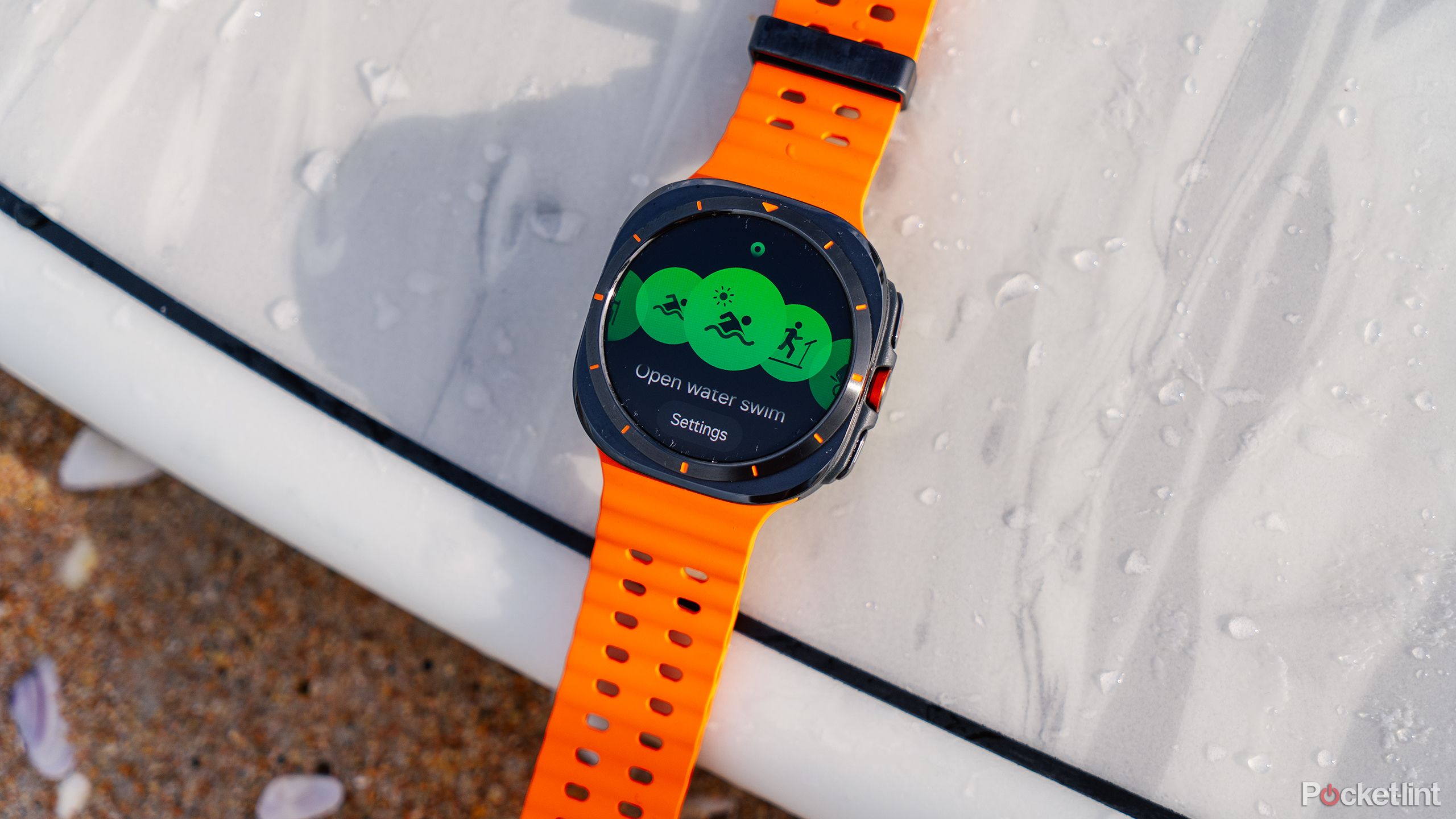 The Samsung Galaxy Watch Ultra rests on a surfboard on sand. 