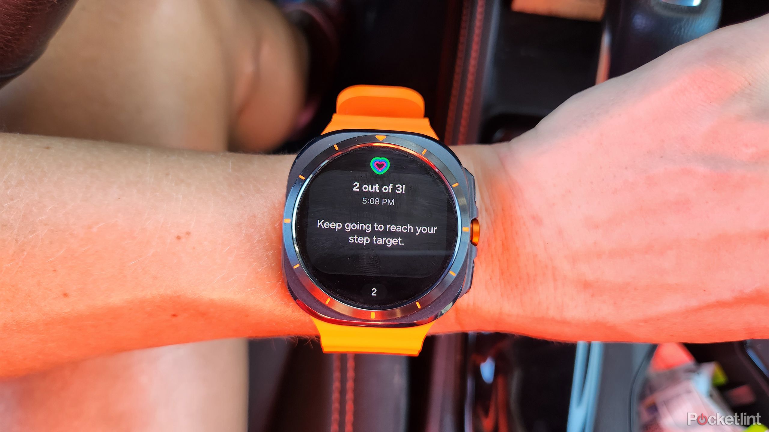 A wrist with the Samsung Galaxy Watch Ultra watch is held above a leg with the steps goal displayed. 