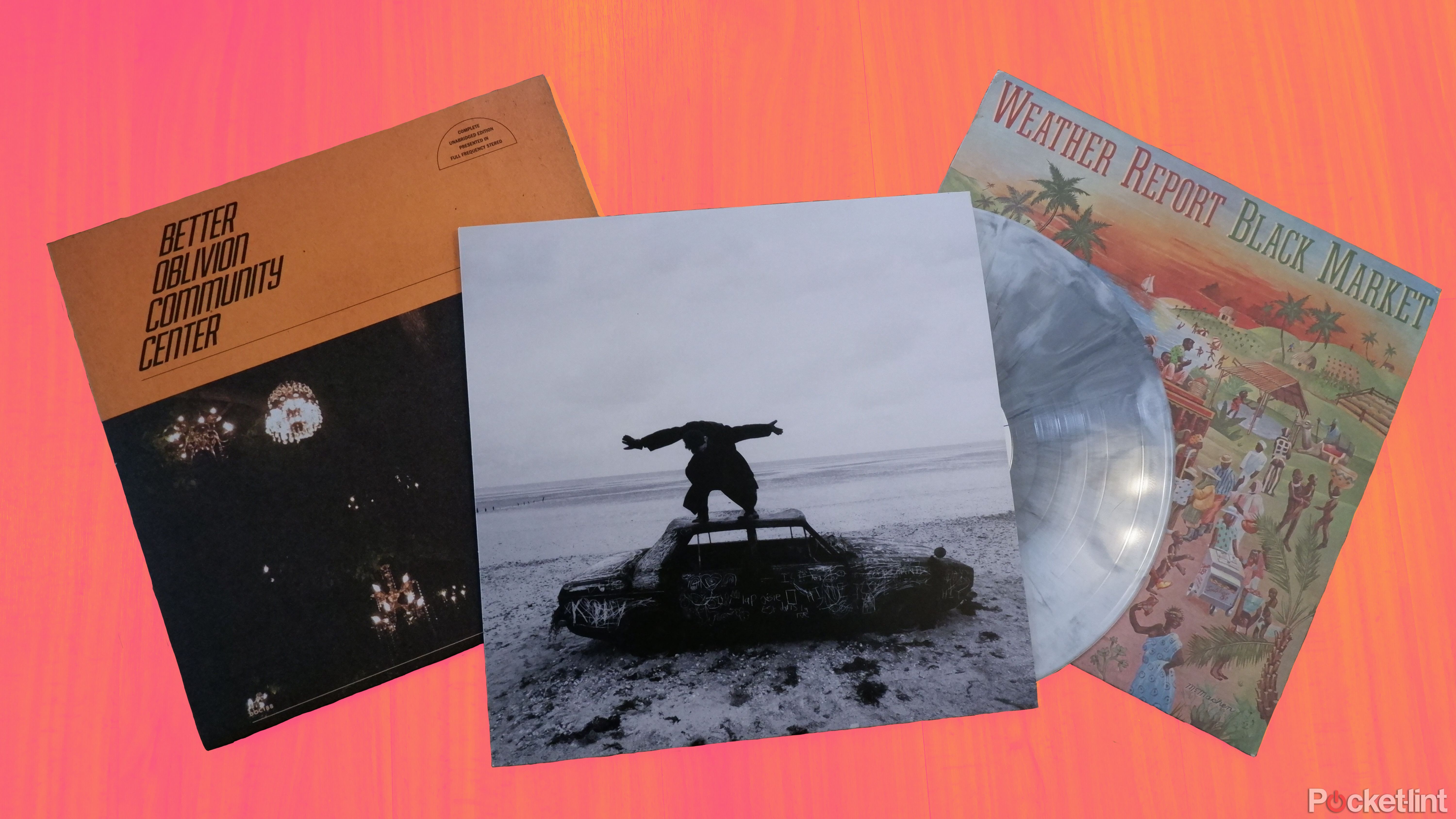 A Better Oblivion Community Center, Weather Report, and The 1975 record on a wooden surface, with The 1975 record peeking out from its packaging.