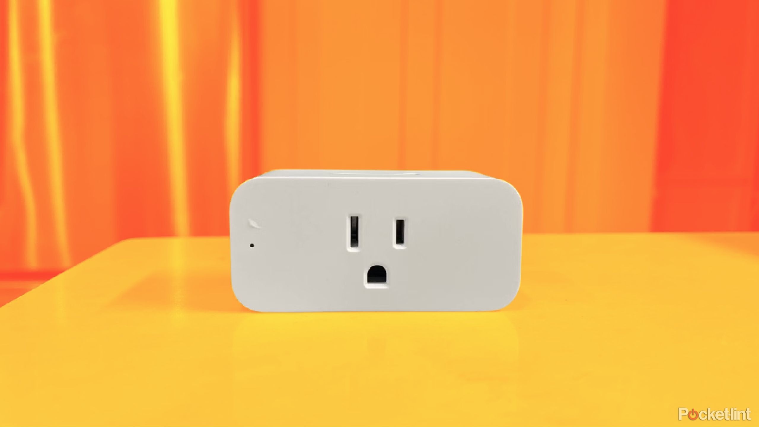 A smart plug sitting on a table on a colored background