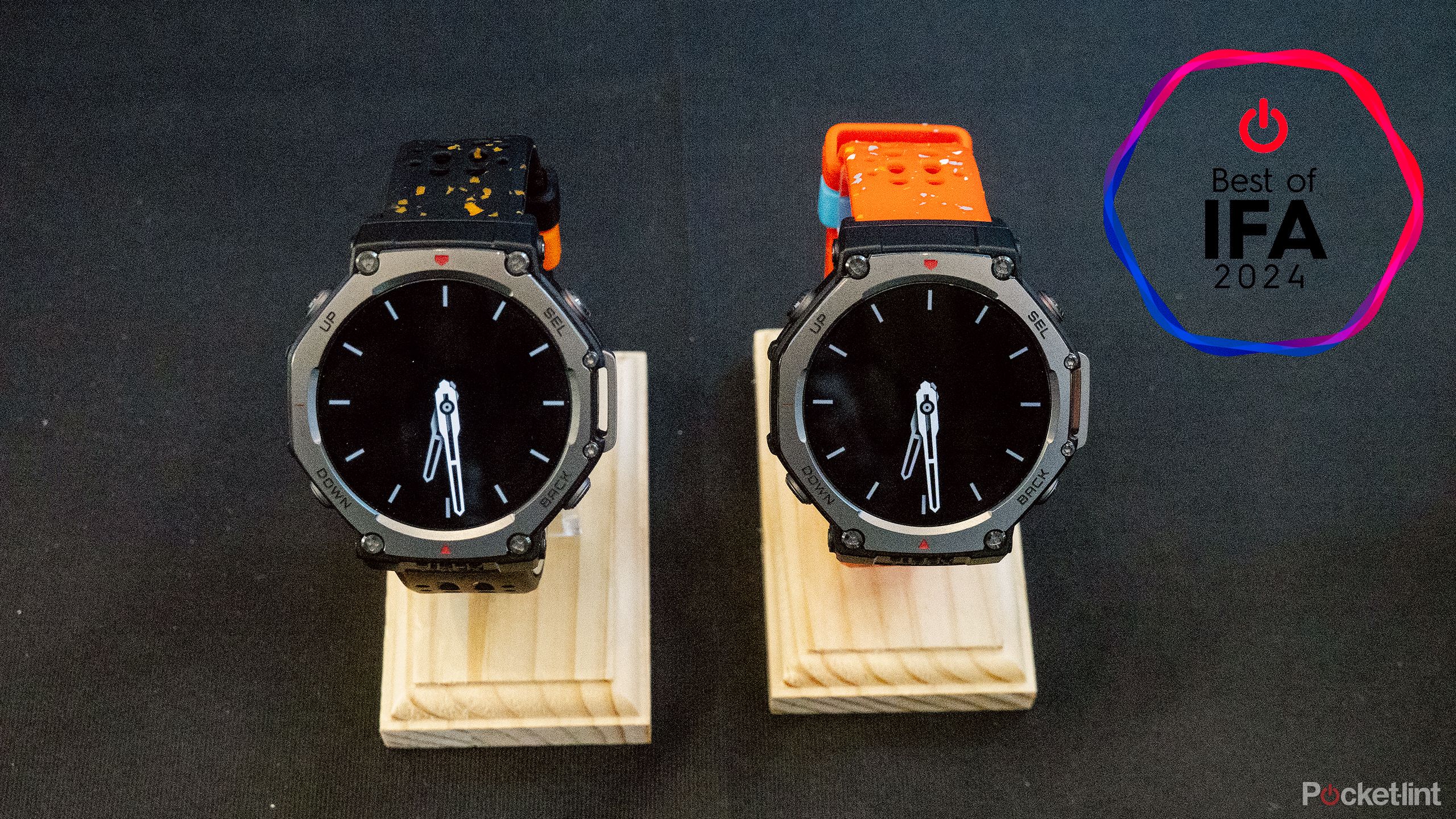 Two Amazfit T-Rex 3 watches sit on stands on a black table. 