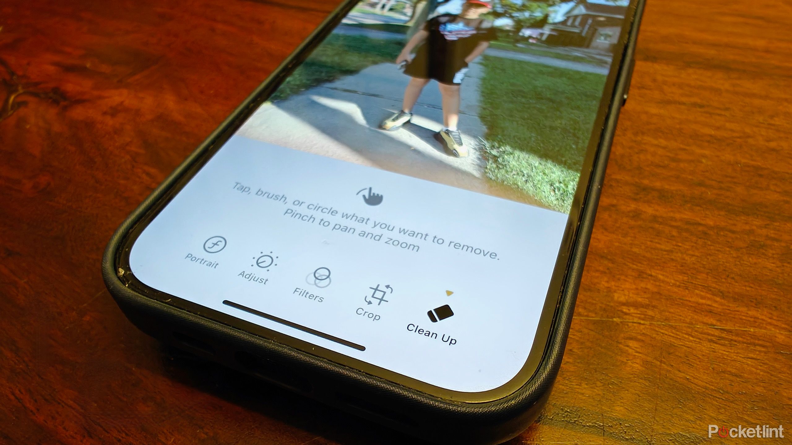 An iPhone on a table showing a photo and the Apple Clean Up menu for editing the image.