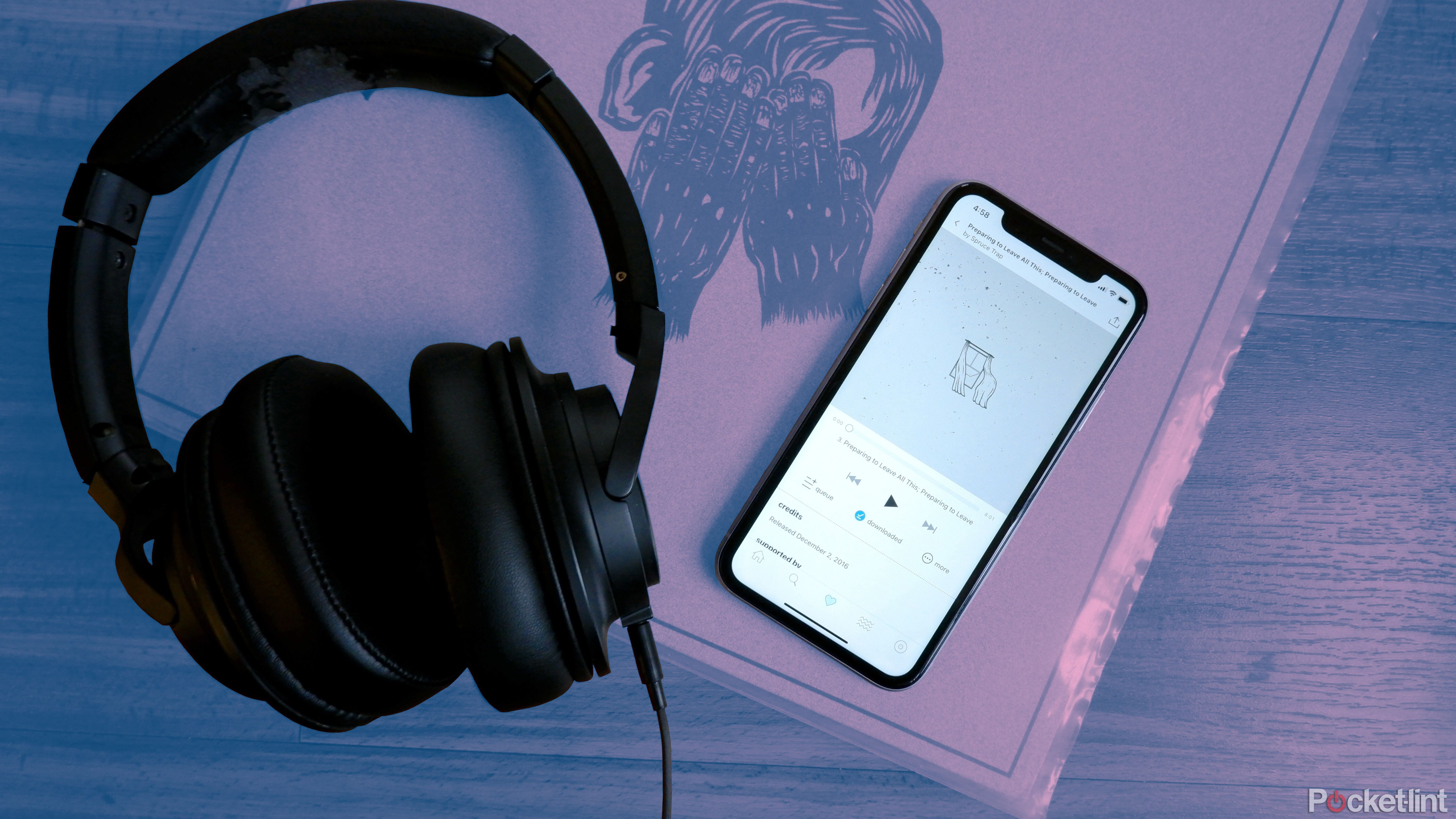 A pair of Audio-Technica headphones beside a phone streaming a song from Bandcamp, on top of a record