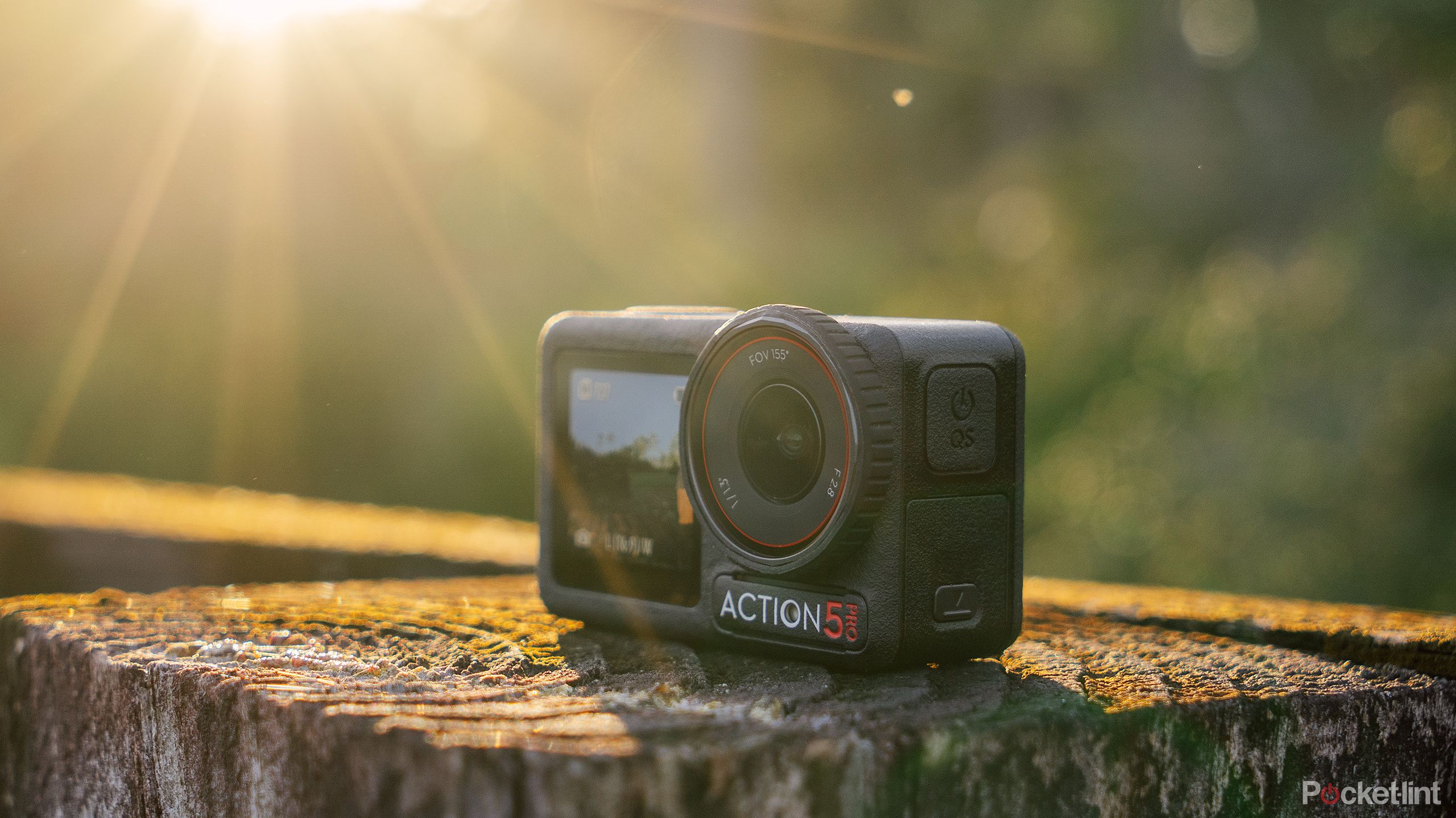 The DJI Osmo Action 5 Pro sits on a weathered fence post with sun rays shining down on it. 