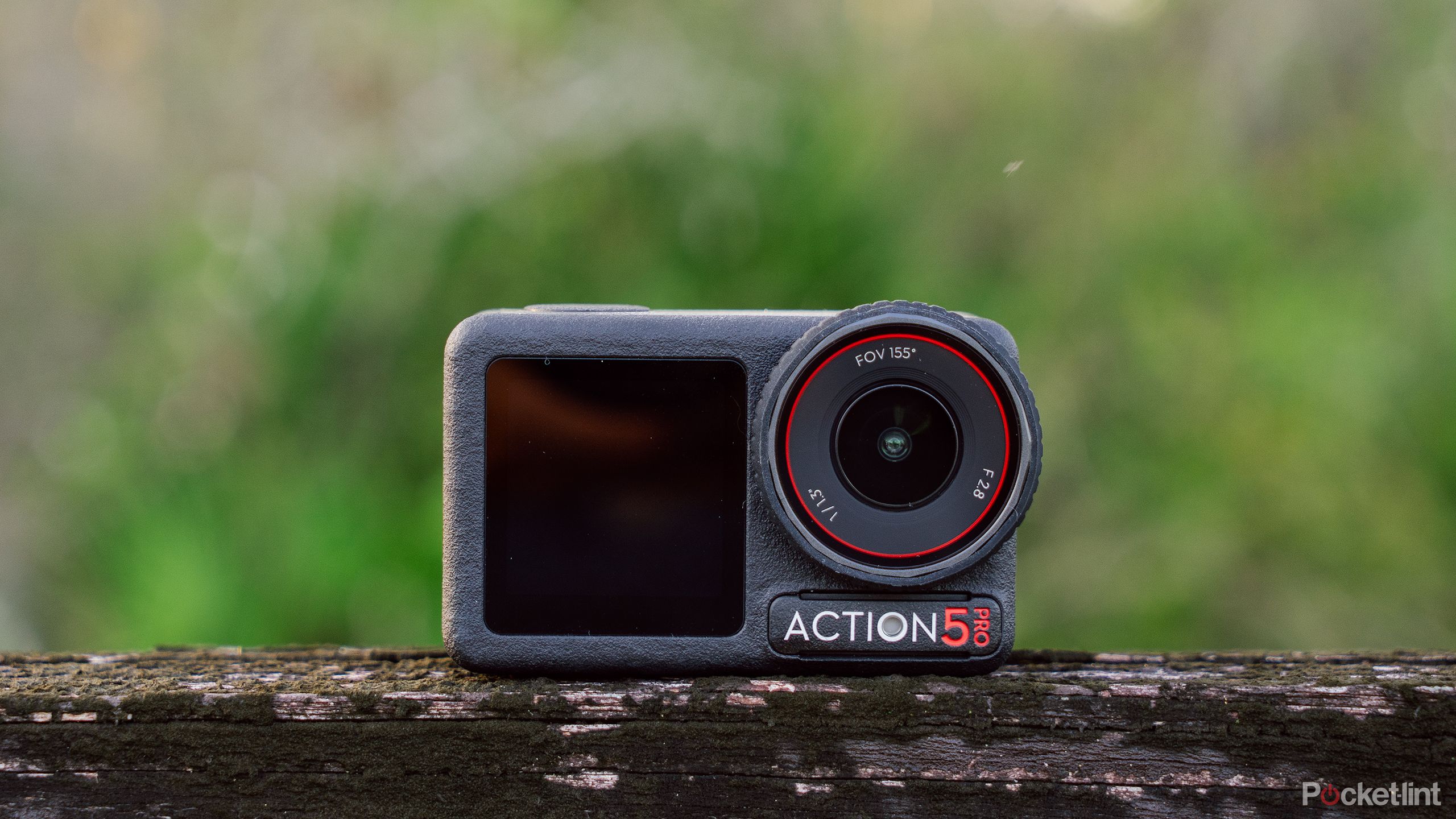 The DJI Osmo Action 5 Pro sits on a weathered fence in front of a blurred green background. 