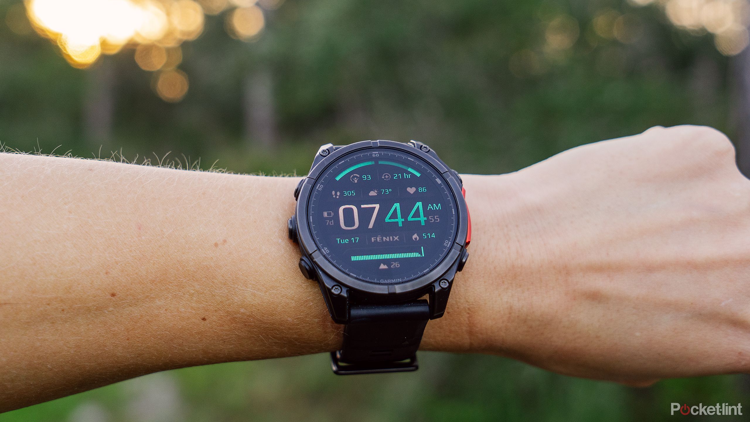 A wrist with the Garmin Fenix 8 on is held in front of a blurred forest. 