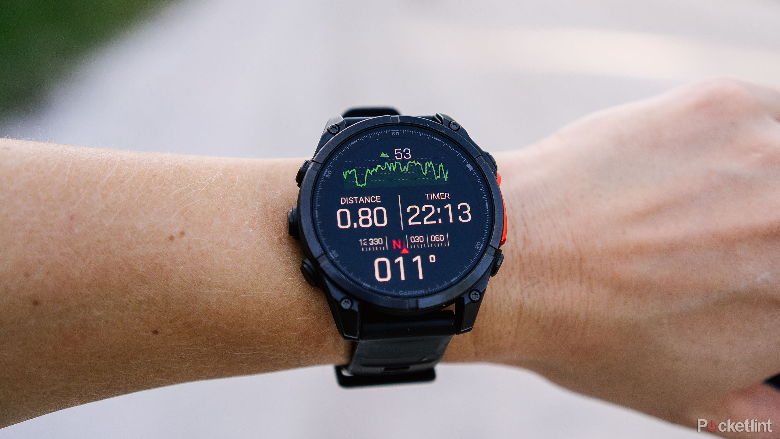 The Garmin Fenix 8 is on a wrist held in front of a blurred gravel road. 