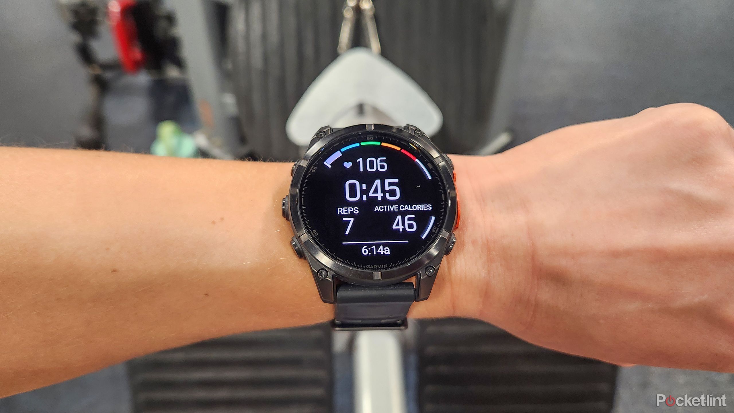 A wrist with the Garmin Fenix 8 is held in front of a weight machine. 