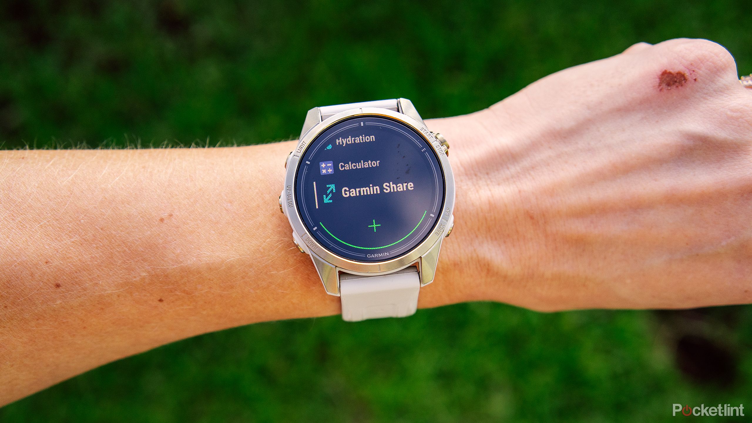 A wrist with the Garmin epix Pro Gen 2 Sapphire is held above blurred green grass with the Garmin Share tool on the display. 