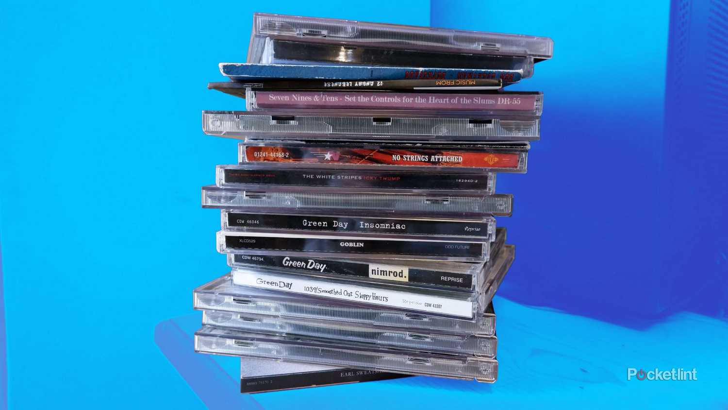 A stack of CDs in cases on a wooden desk.