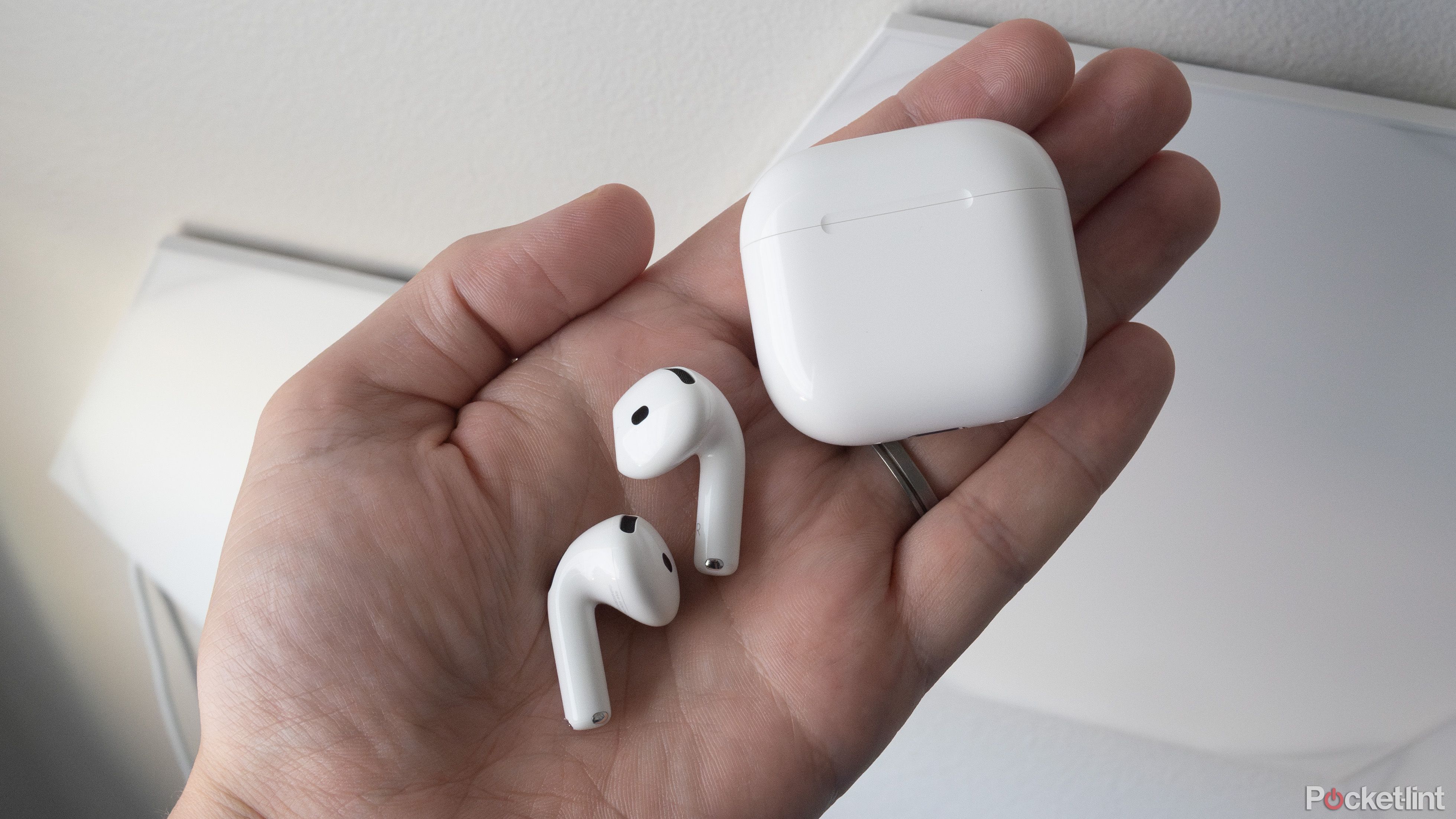 The AirPods 4 in a hand beside their case