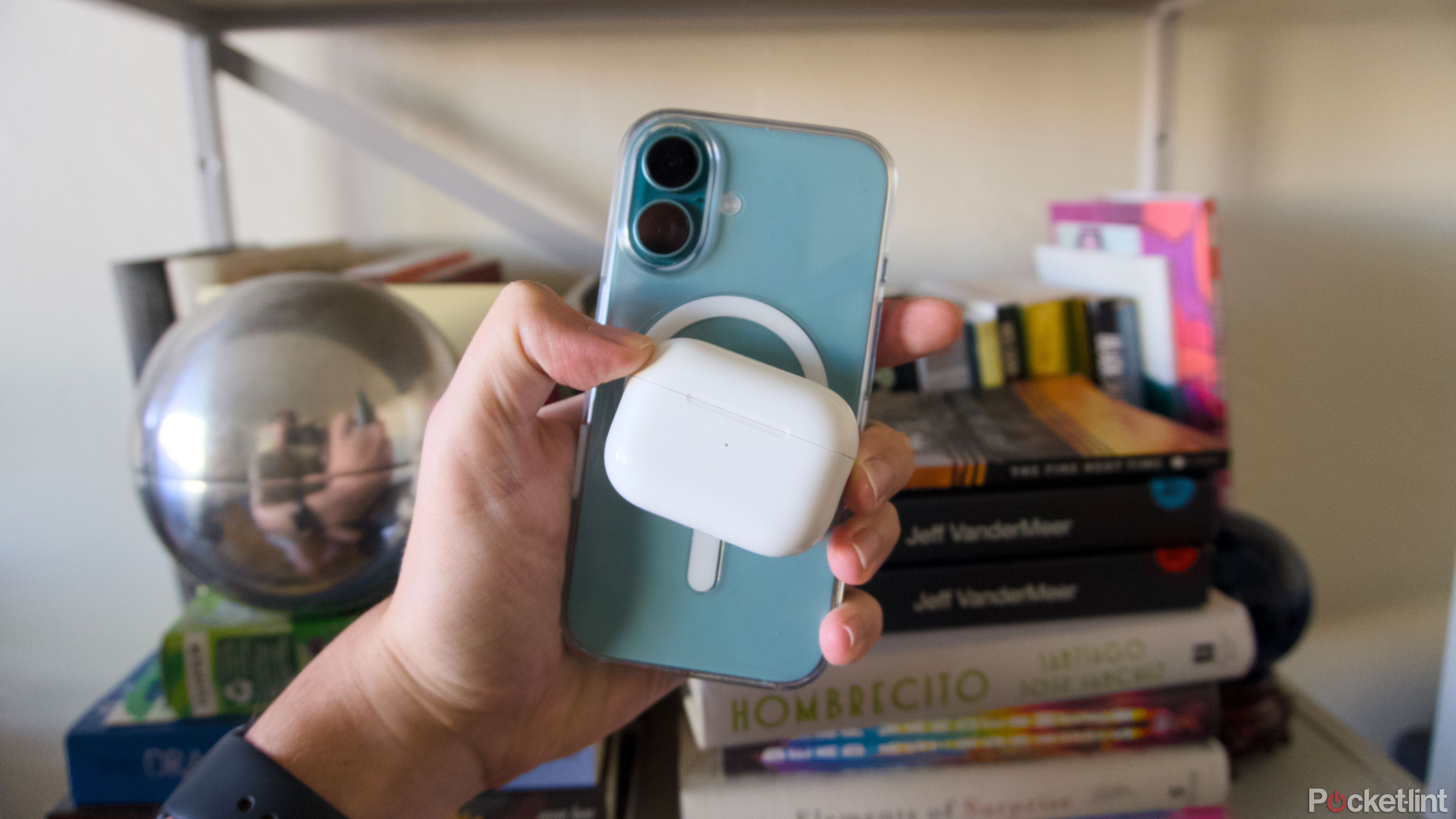 An AirPods Pro charging case held against the back of a teal iPhone 16.