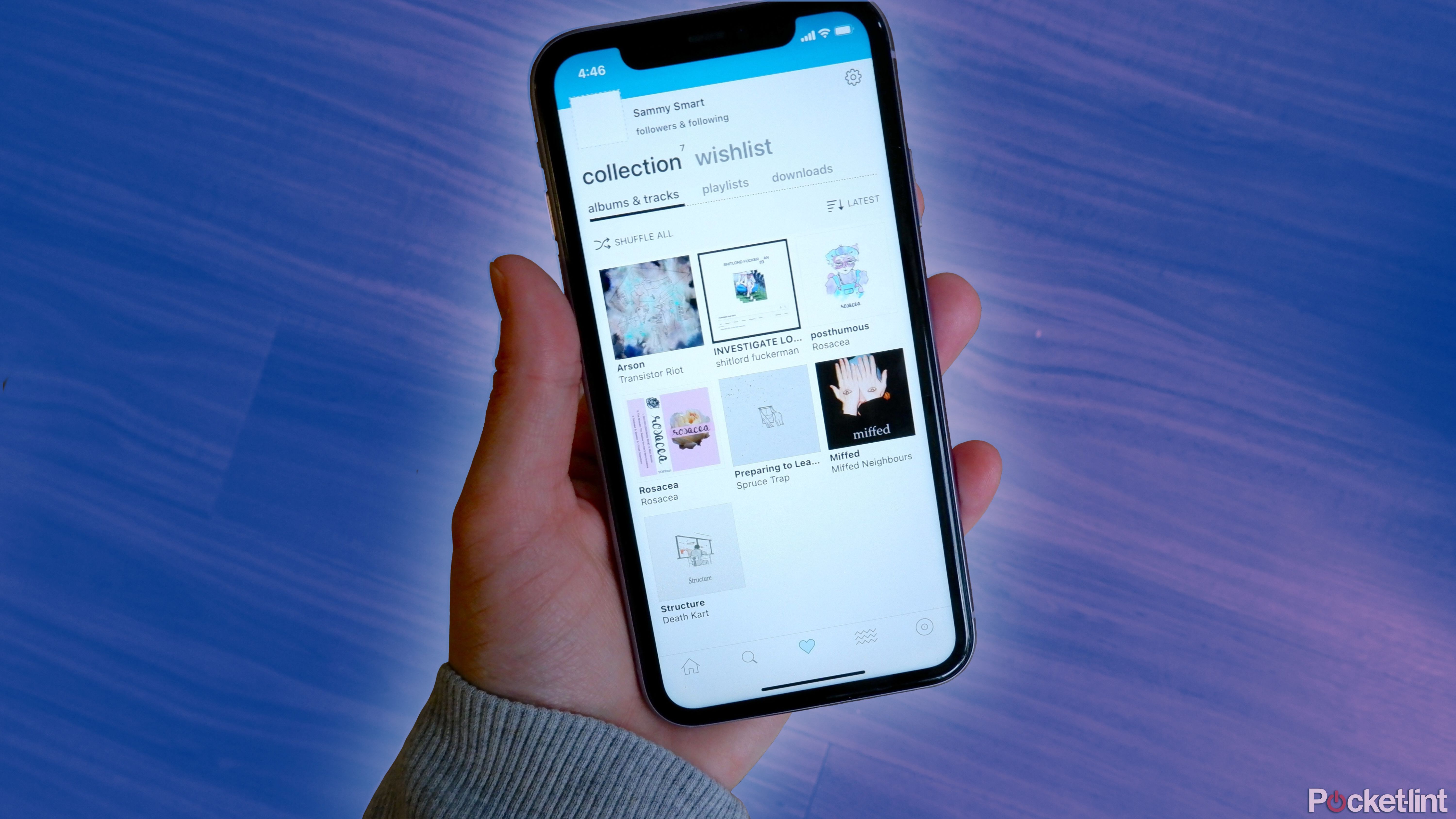 An iPhone with the Bandcamp app open being held in a hand above a wooden floor