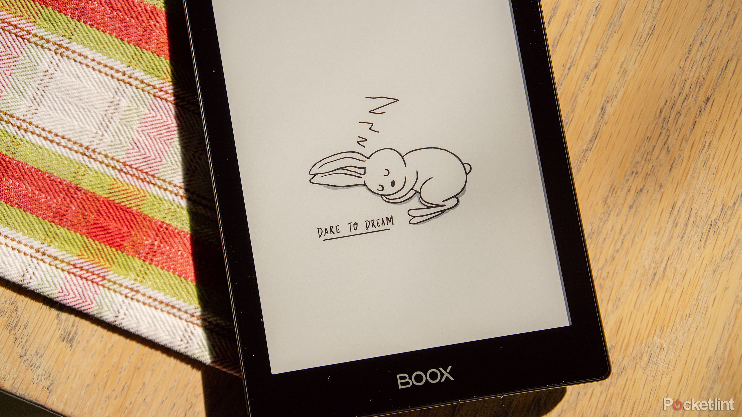 The Boox Go 6 e-reader sits on a wood table with the sleeping graphic on the display. 