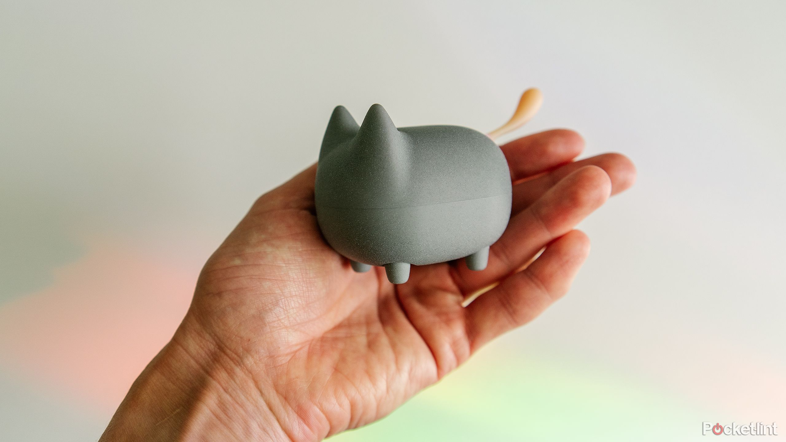 A hand holds the Gingo KItty Speaker over a white desk with rainbow light on it. 