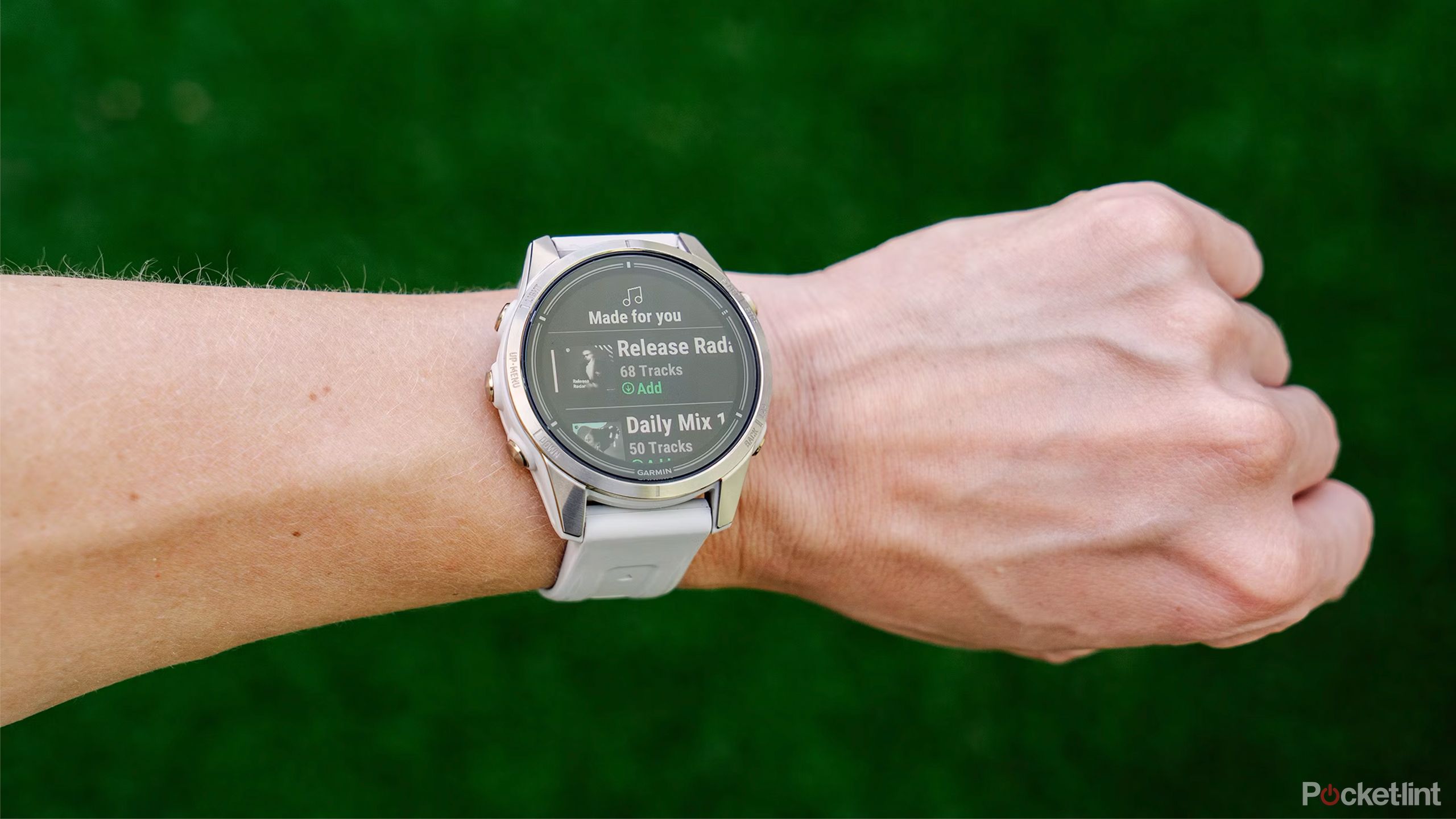 A wrist with the Garmin epix Pro Gen 2 with Spotify on the display is held above a blurred green background. 