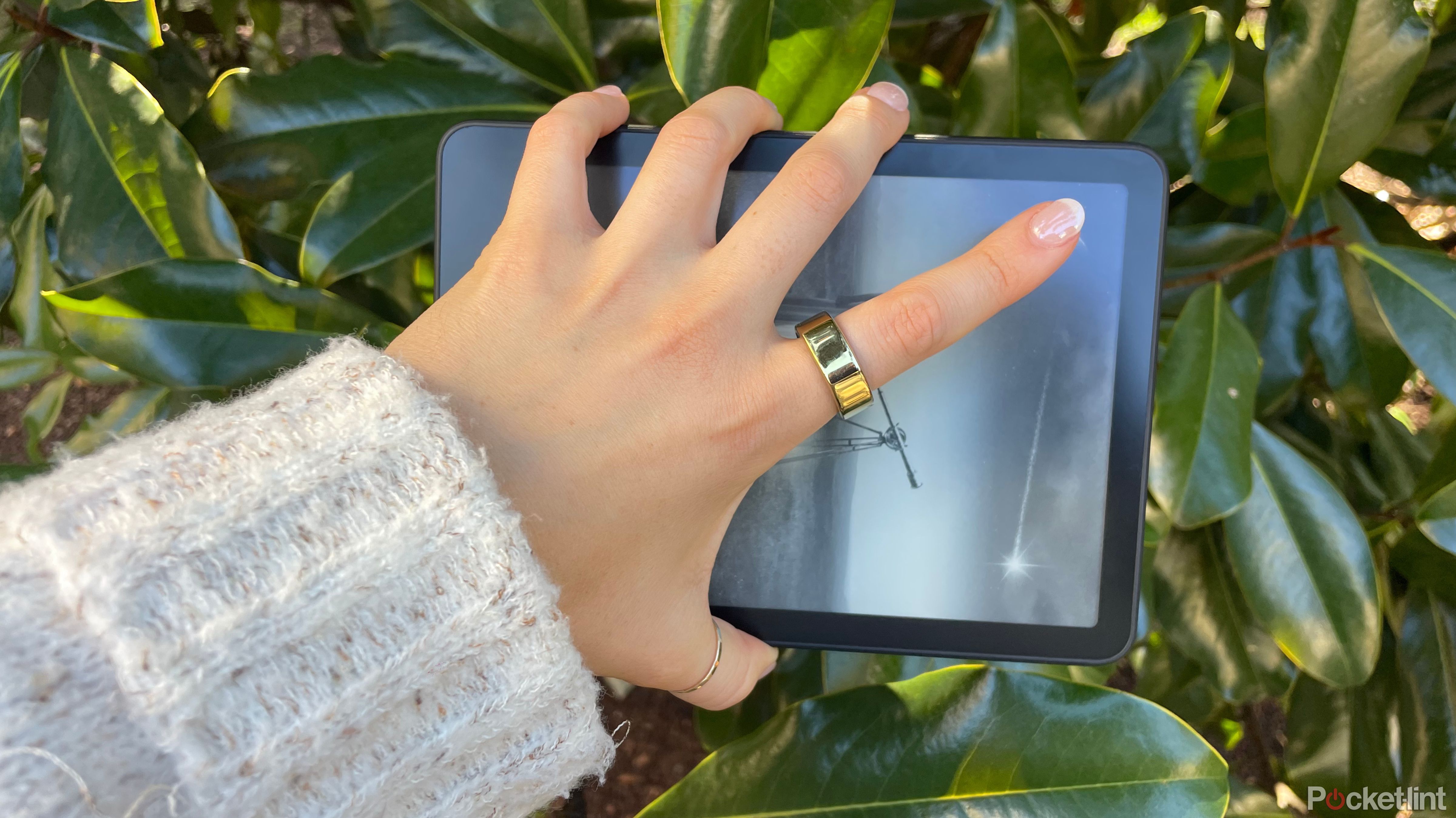 A woman holding a Kindle Paperwhite in front of foliage. 