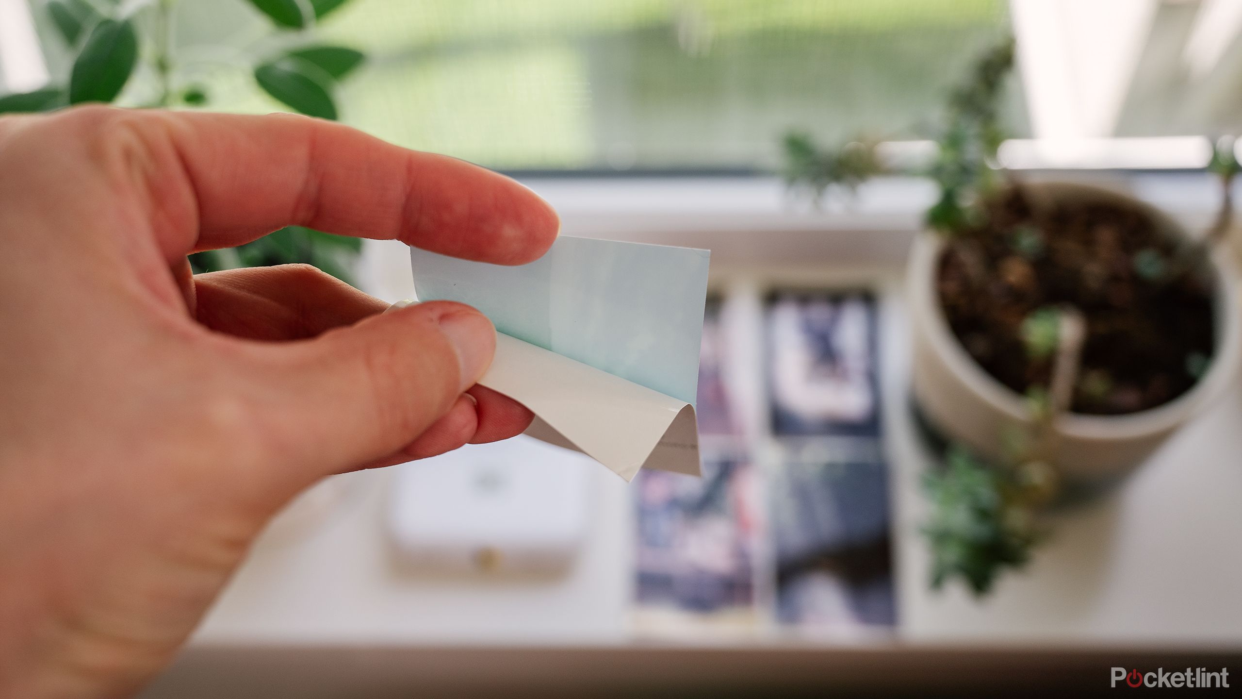 A hand peels off the paper backing on the ZINK photo paper sticker. 