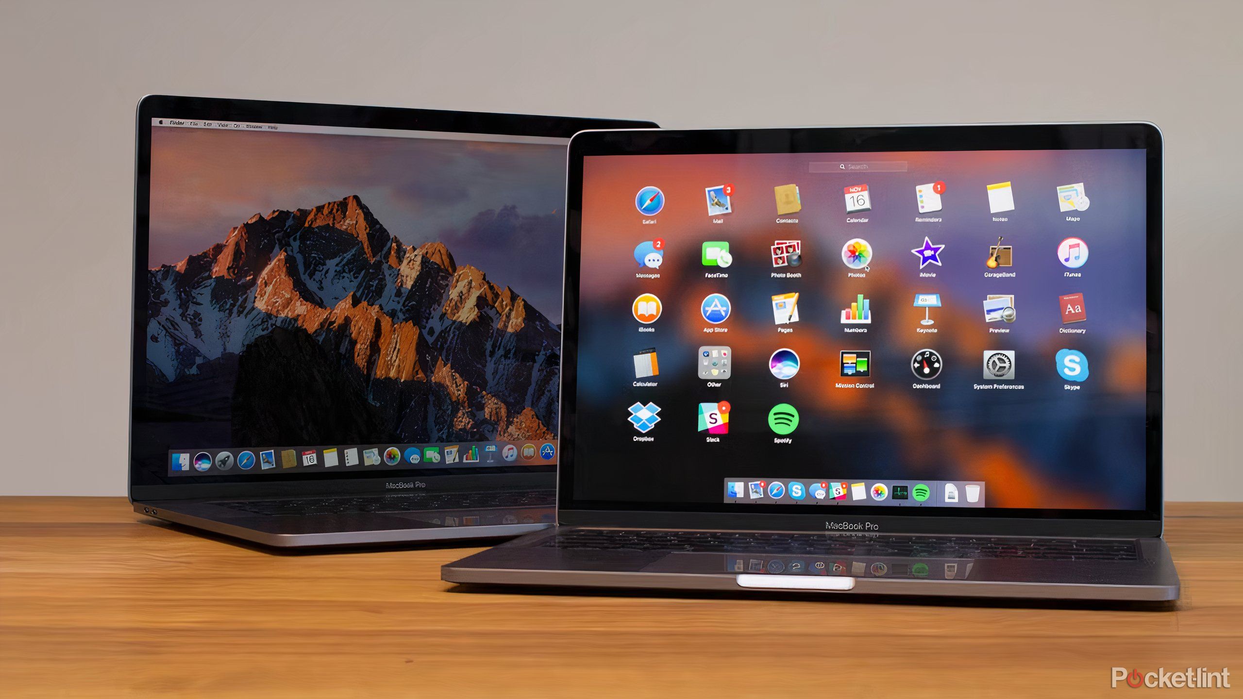 Two gray MacBook Pros with Touch Bars sitting on a wooden table.