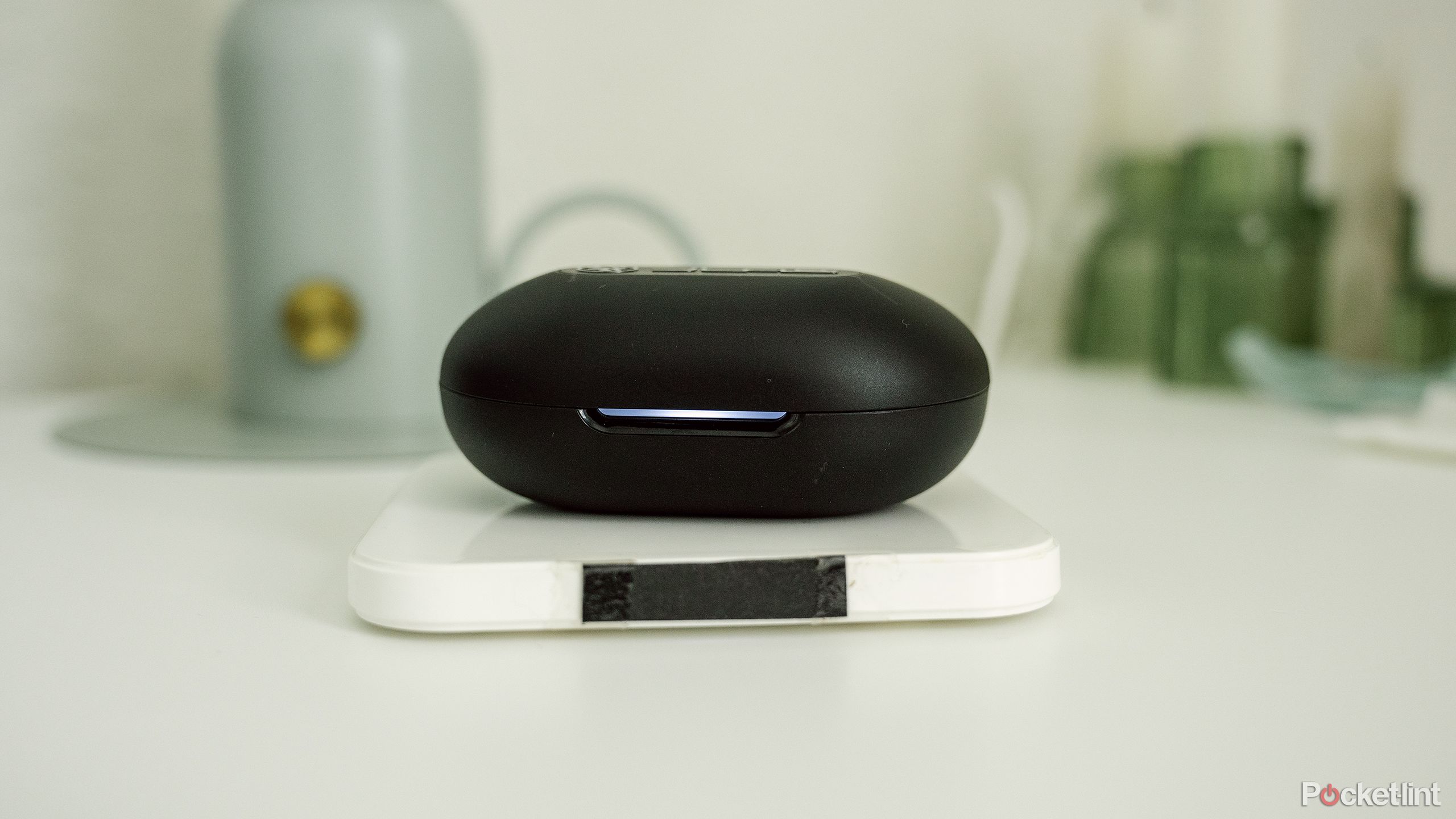 The JLab Epic Sport ANC 3 earbuds case sits on a wireless charger on a white nightstand. . 