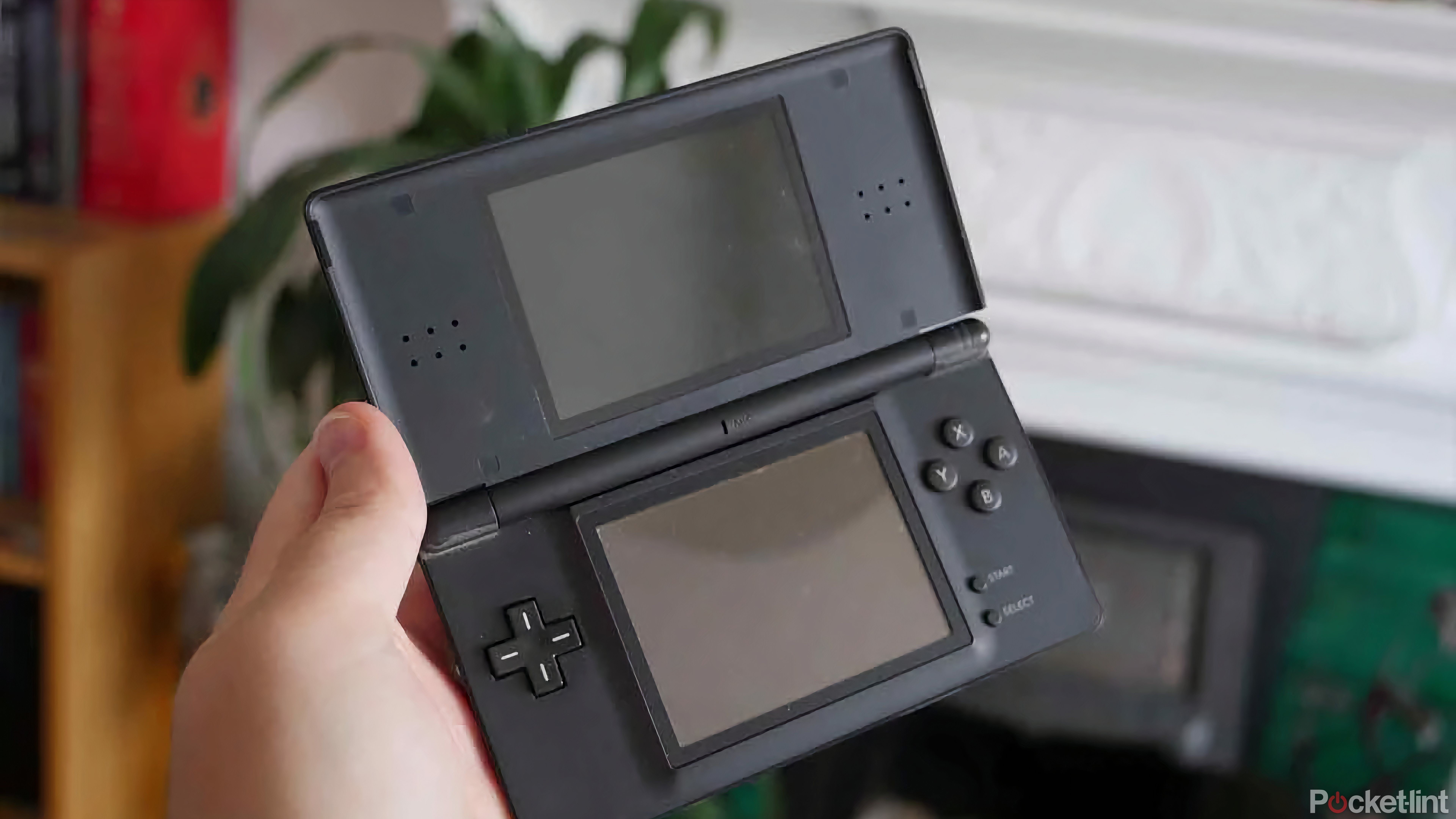 A hand holding a black Nintendo DS Lite with its screens off.