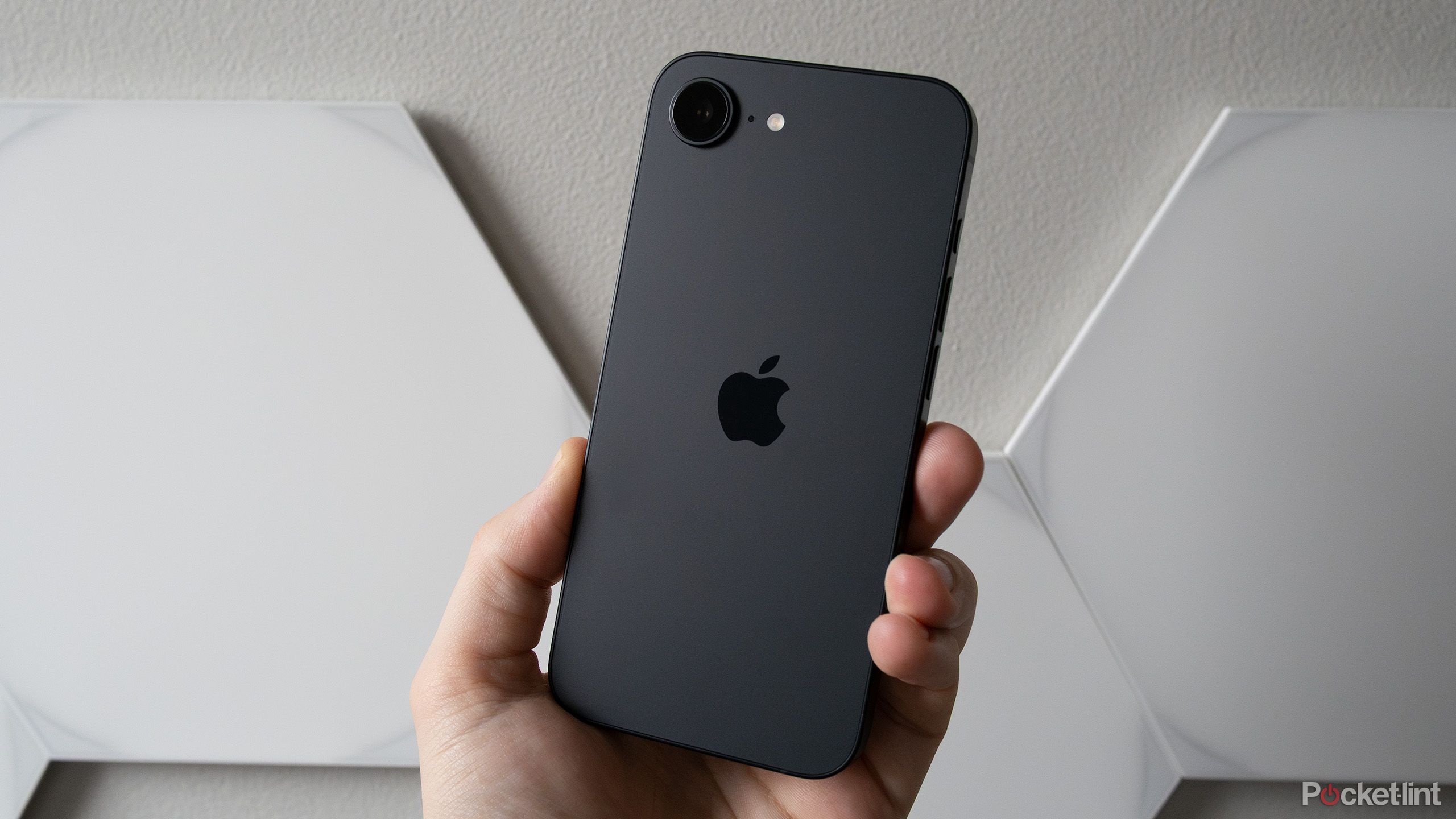 Person holding black iPhone 16e against a white background.