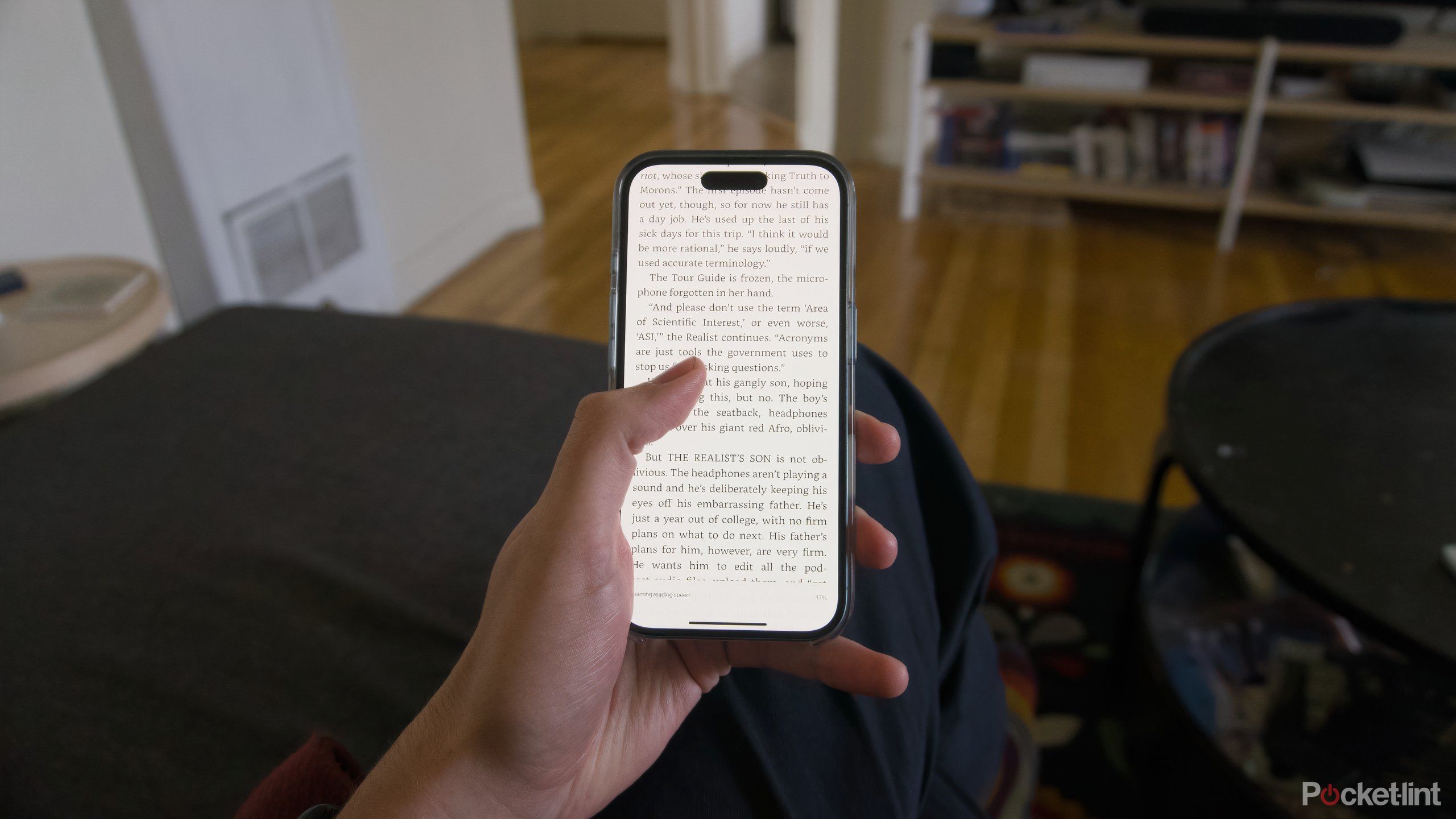 A hand holding an iPhone and scrolling through a book.