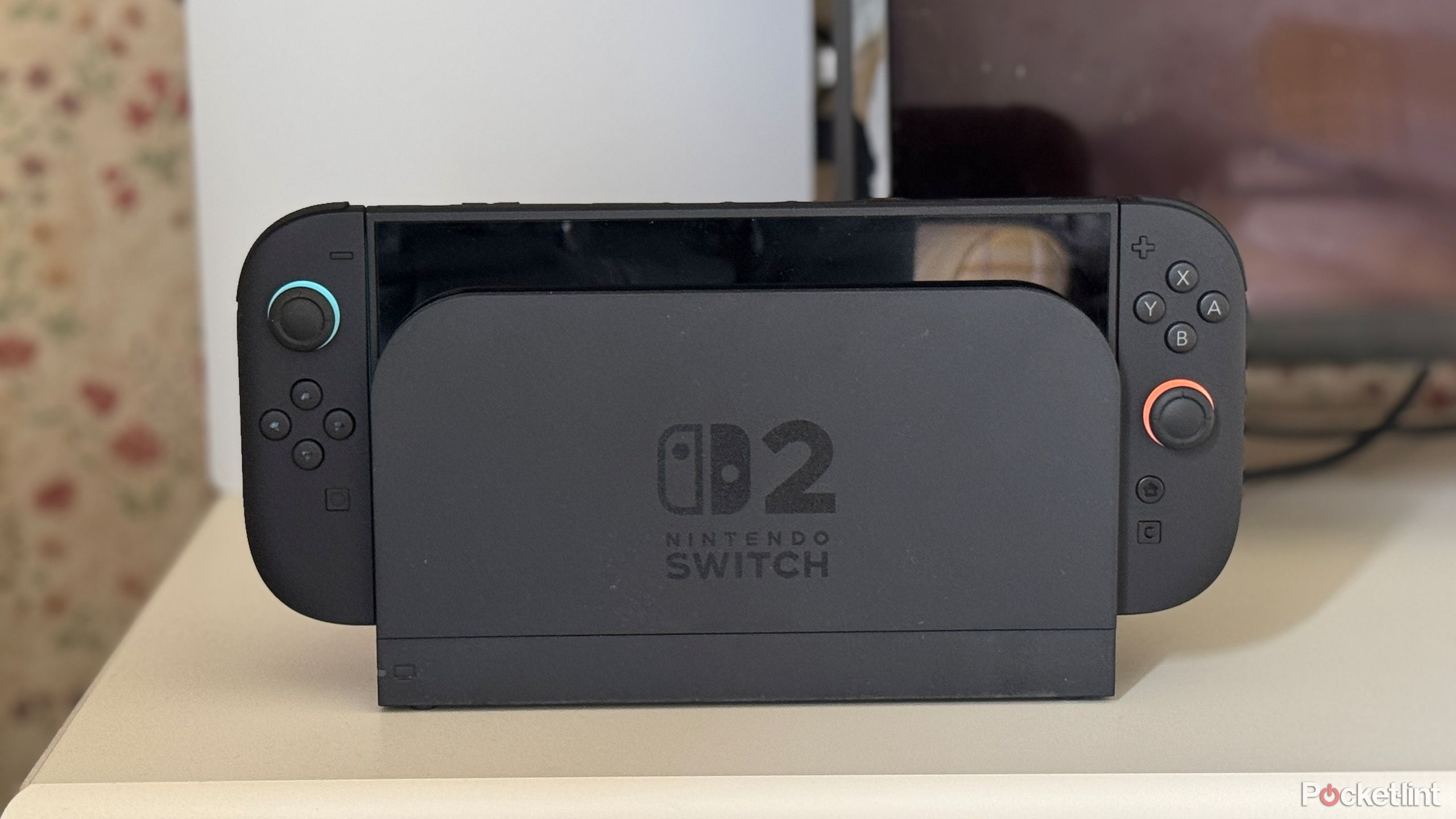 A Nintendo Switch 2 docked with a Playstation 5 and TV in the background.