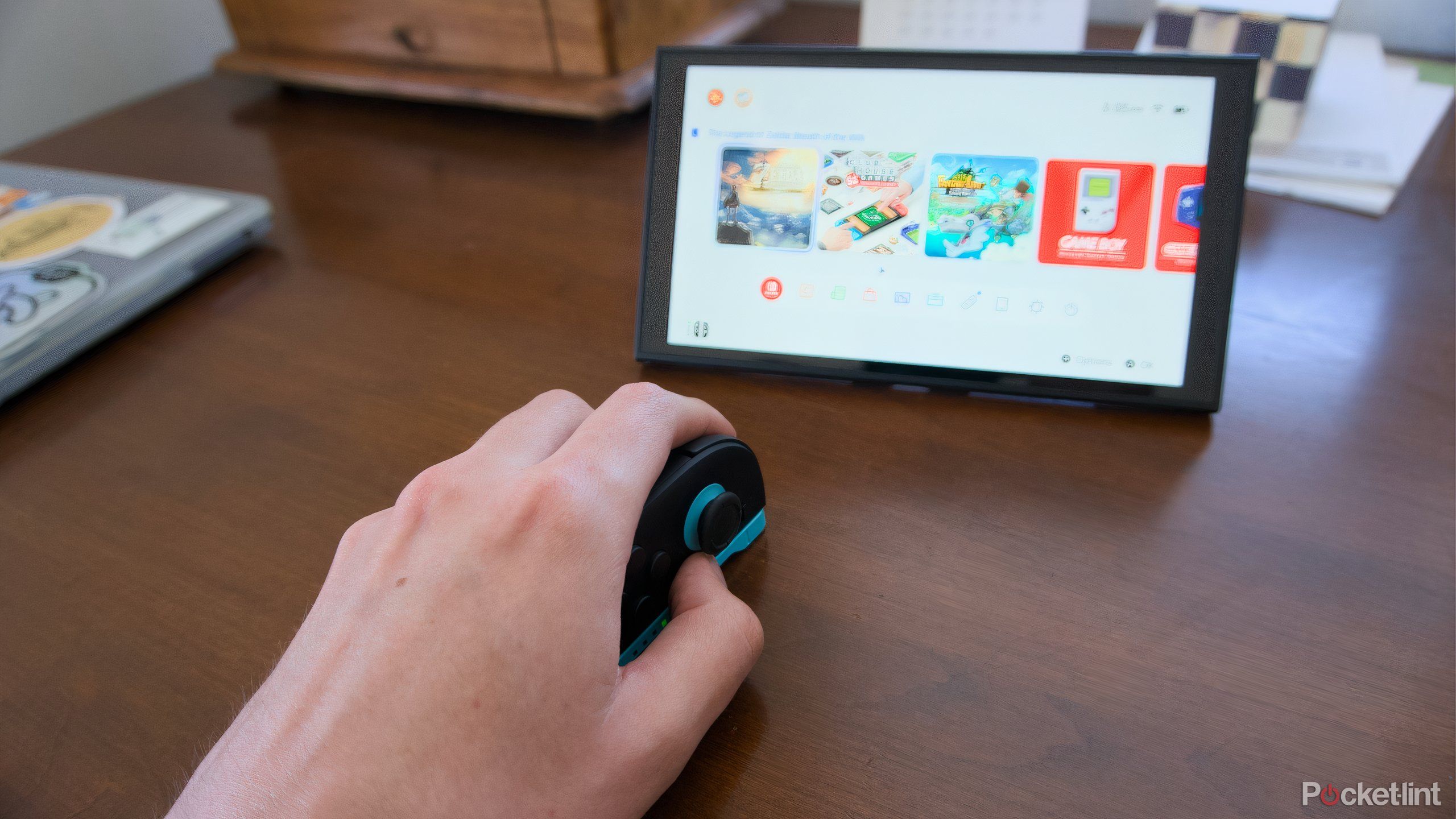 A hand using a Joy-Con 2 like a mouse in front of a Switch 2.