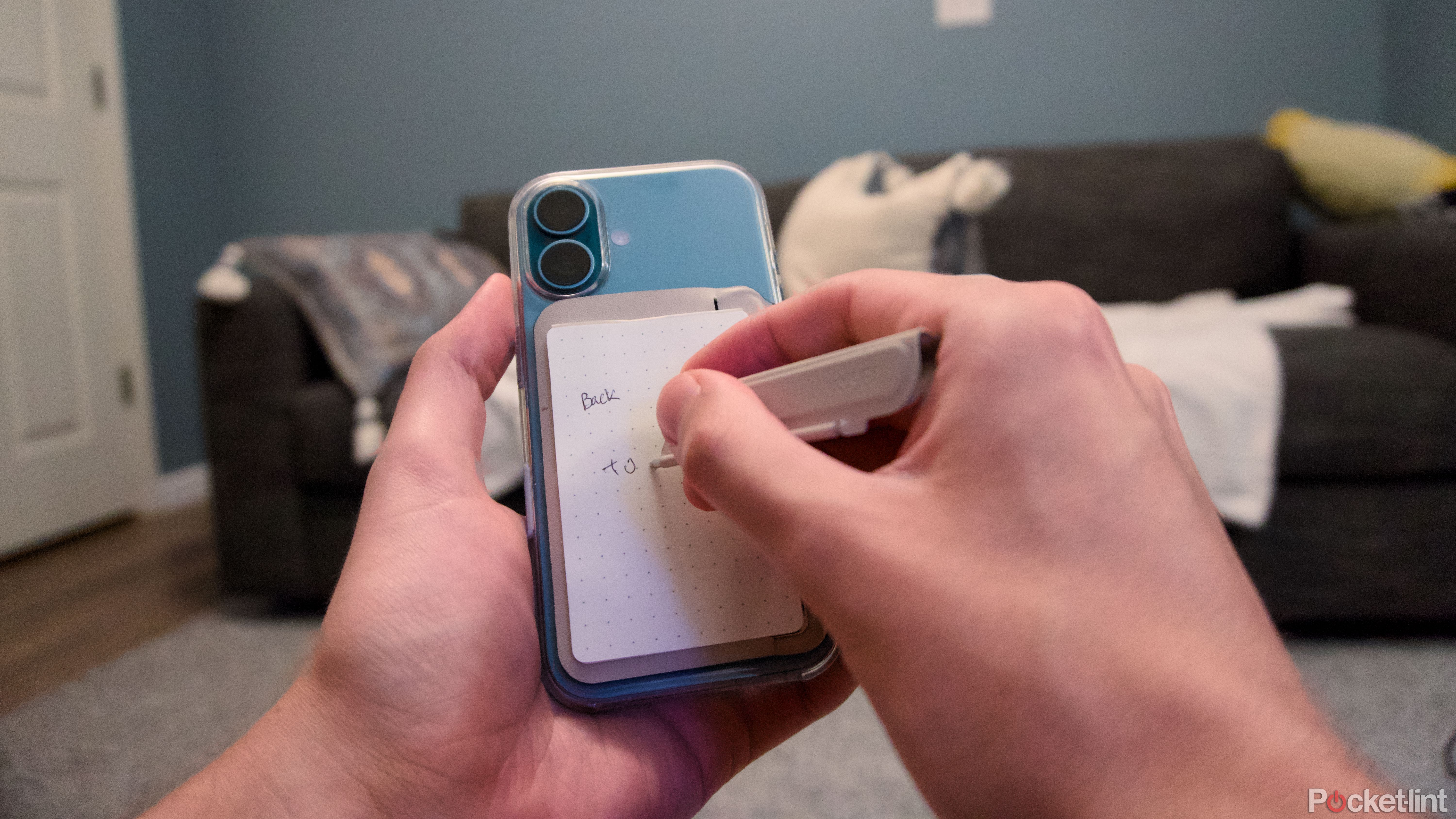 A hand writing on a notepad attached to the back of an iPhone 16.